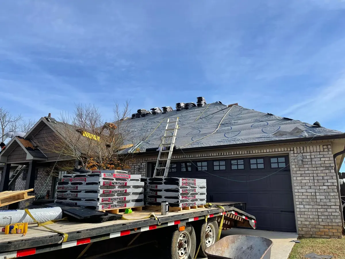 Roof tear-off with new shingle bundles on a trailer in the driveway