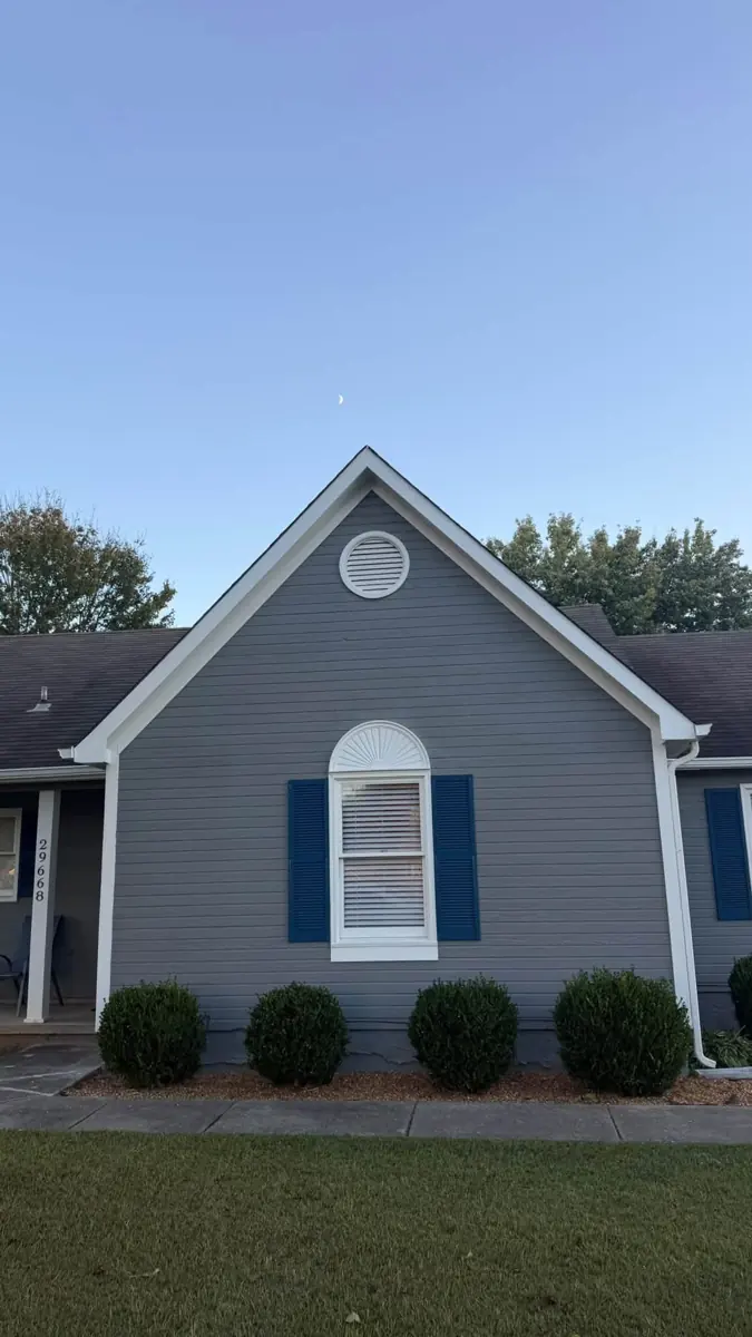 Front gable of a gray home with arched window and trimmed shrubs